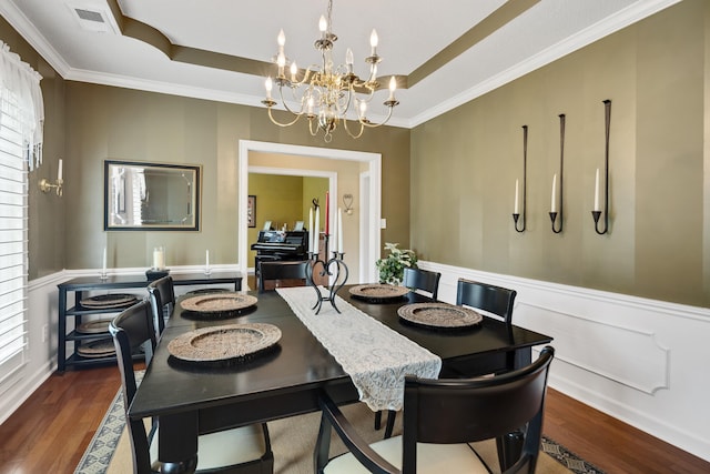dining room with an inviting chandelier, ornamental molding, a raised ceiling, and wood finished floors