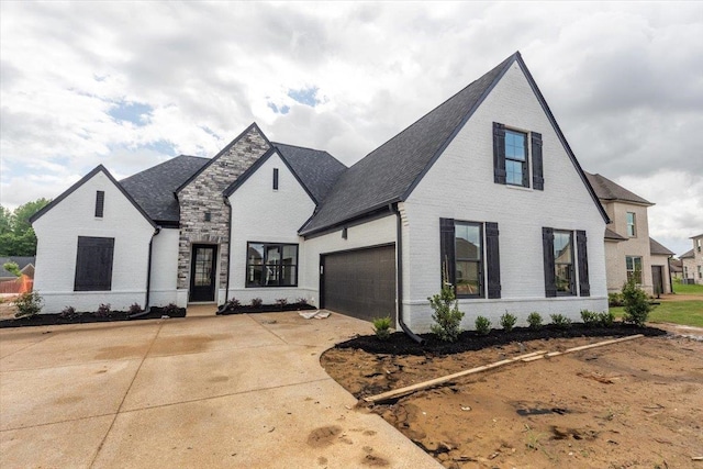 french country inspired facade with concrete driveway, a shingled roof, and brick siding