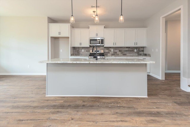 kitchen with an island with sink, white cabinets, baseboards, appliances with stainless steel finishes, and decorative backsplash