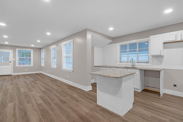 kitchen featuring a sink, light wood finished floors, white cabinets, light stone countertops, and baseboards