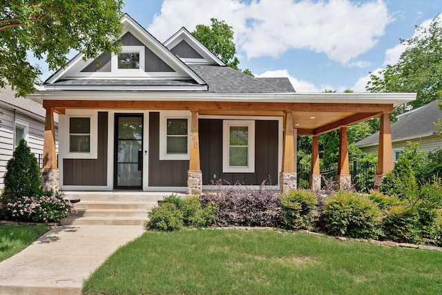 craftsman house with stone siding, a front lawn, board and batten siding, a porch, and roof with shingles