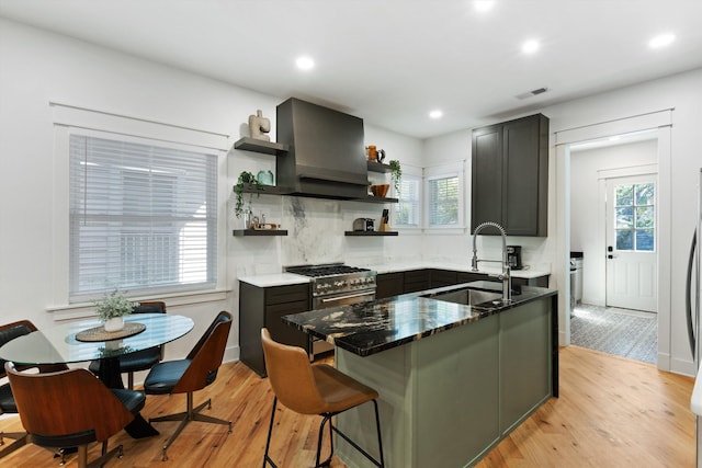 kitchen with dark stone countertops, open shelves, a sink, visible vents, and wall chimney range hood