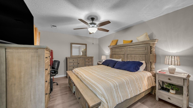 bedroom with wood finished floors, a textured ceiling, visible vents, ceiling fan, and baseboards