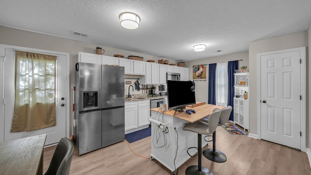 kitchen featuring light wood finished floors, stainless steel fridge, white cabinetry, visible vents, and a textured ceiling