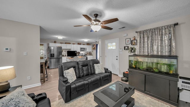 living room with light wood finished floors, visible vents, baseboards, and ceiling fan