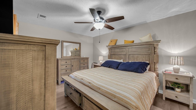 bedroom featuring a ceiling fan, visible vents, a textured ceiling, and wood finished floors