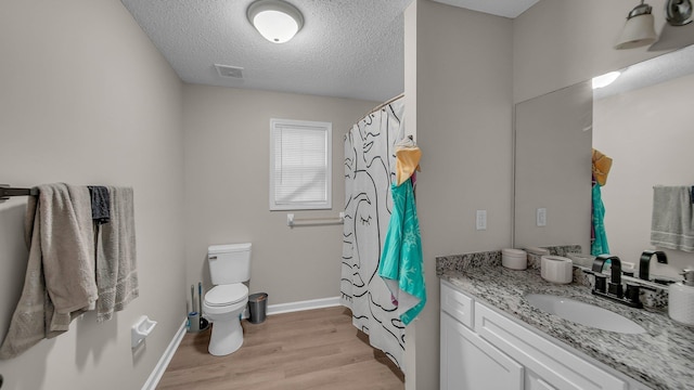 bathroom with toilet, wood finished floors, a textured ceiling, visible vents, and vanity