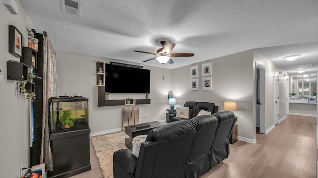 home theater room featuring a ceiling fan, a textured ceiling, baseboards, visible vents, and light wood-type flooring