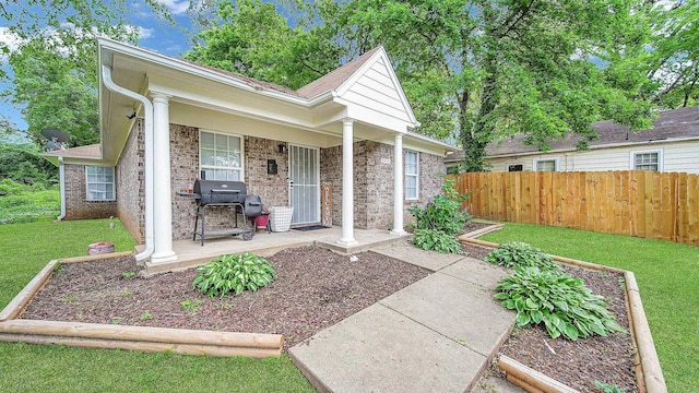 view of front of house with a front lawn, brick siding, a porch, and fence