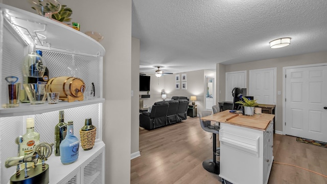 kitchen with wood finished floors, ceiling fan, white cabinetry, a kitchen bar, and wooden counters