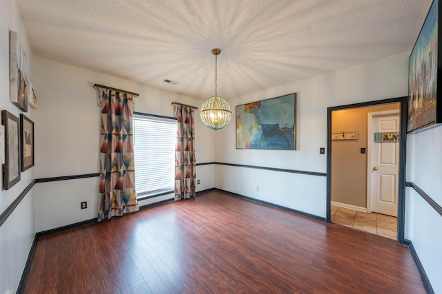 unfurnished room with wood finished floors, a textured ceiling, visible vents, baseboards, and a chandelier