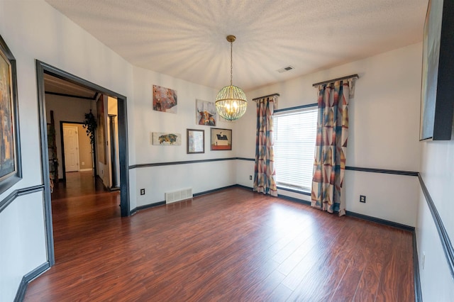 spare room with visible vents, wood finished floors, baseboards, and a notable chandelier