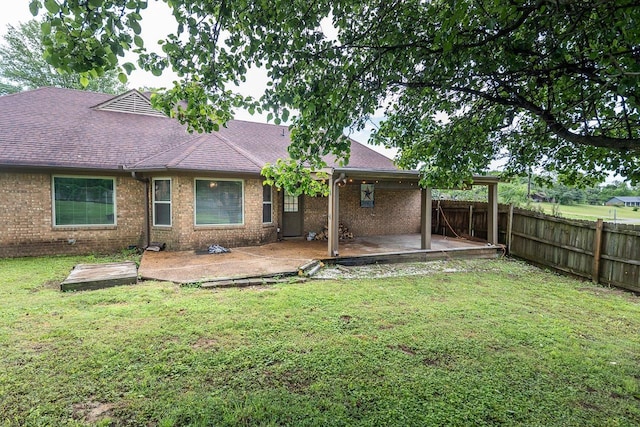 back of house featuring a patio, fence, a yard, roof with shingles, and brick siding
