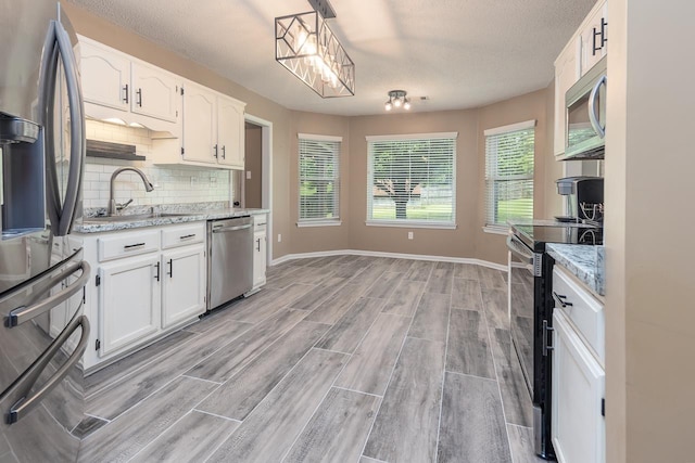 kitchen featuring a sink, tasteful backsplash, appliances with stainless steel finishes, white cabinetry, and light wood-style floors
