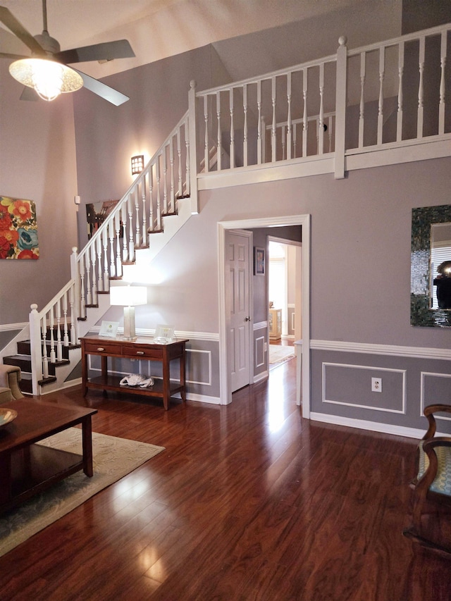 stairway with a decorative wall, wood finished floors, a towering ceiling, a ceiling fan, and wainscoting