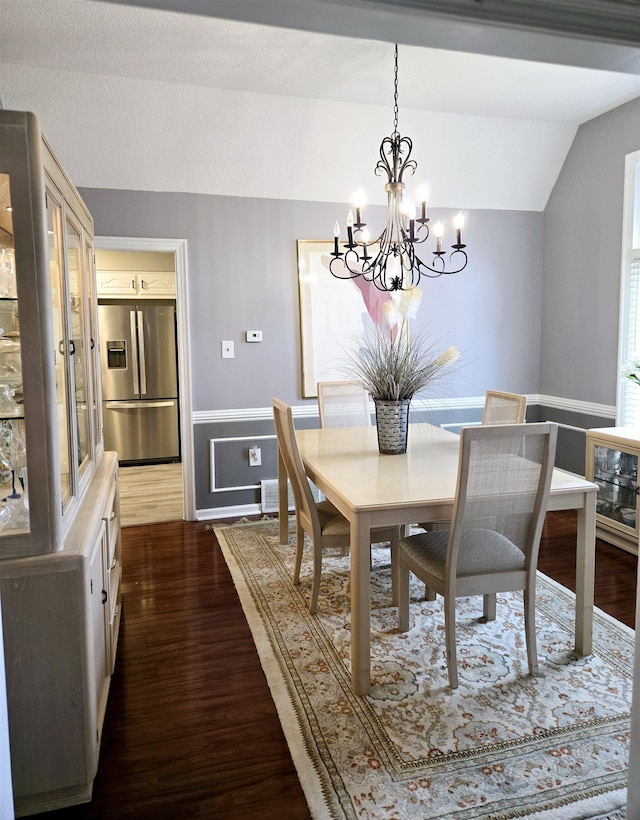 dining room with vaulted ceiling, a chandelier, dark wood-style flooring, and a wainscoted wall
