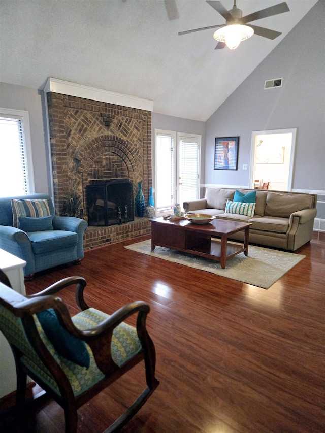 living room featuring ceiling fan, a brick fireplace, visible vents, and wood finished floors