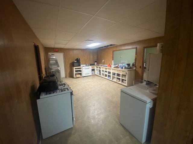 basement featuring fridge, a drop ceiling, and wood walls