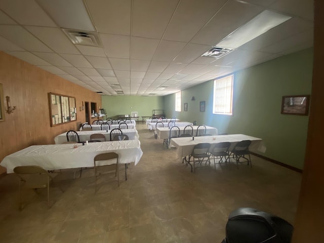 dining area with a drop ceiling, wooden walls, and visible vents