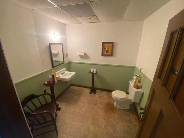 half bath featuring toilet, a paneled ceiling, and a sink