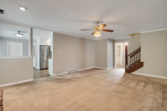 unfurnished living room with light colored carpet, a ceiling fan, ornamental molding, baseboards, and stairway
