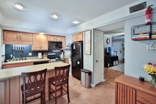 kitchen featuring light brown cabinetry, visible vents, a sink, black appliances, and light countertops