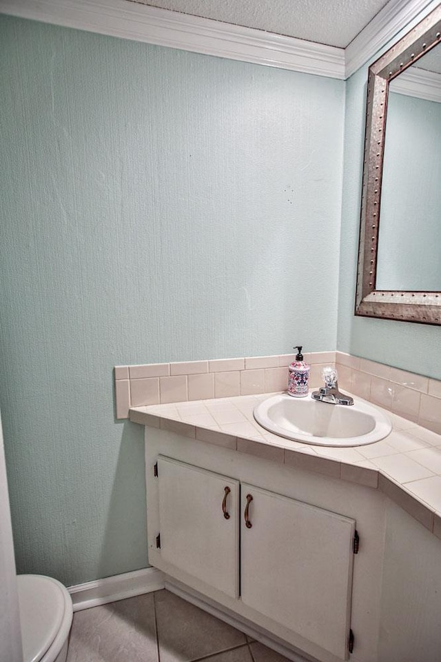 half bath with toilet, vanity, a textured ceiling, crown molding, and tile patterned flooring