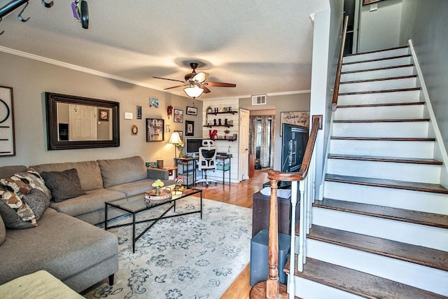 living room with wood finished floors, a ceiling fan, crown molding, stairway, and visible vents