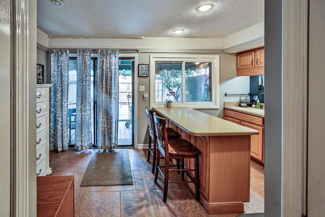 kitchen with a kitchen breakfast bar, a peninsula, a textured ceiling, and light countertops