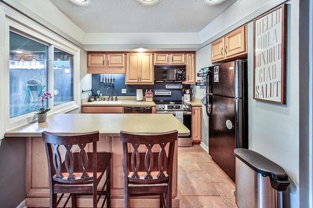 kitchen with a breakfast bar, a textured ceiling, light countertops, and black appliances