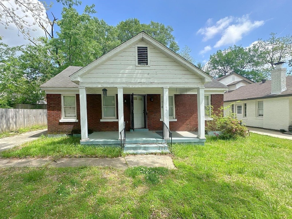 view of front facade with a front lawn, brick siding, fence, and a porch