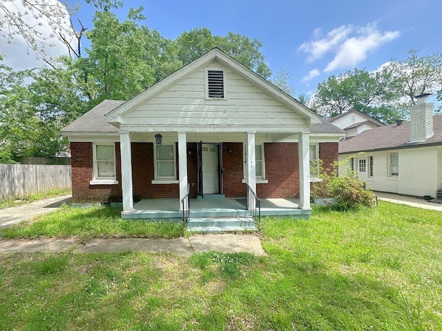 view of front facade with a front lawn, brick siding, fence, and a porch