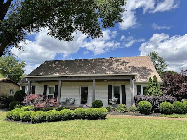 view of front of home with a front lawn, a shingled roof, a porch, and brick siding