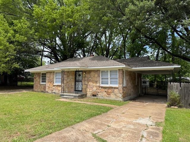 bungalow-style home with driveway, fence, stone siding, a front lawn, and a carport