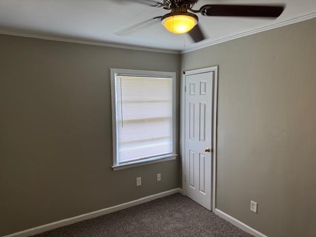 empty room featuring a ceiling fan, baseboards, dark colored carpet, and crown molding