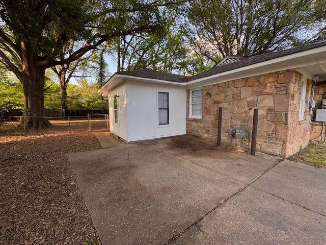 view of property exterior featuring stone siding, a patio, driveway, and fence