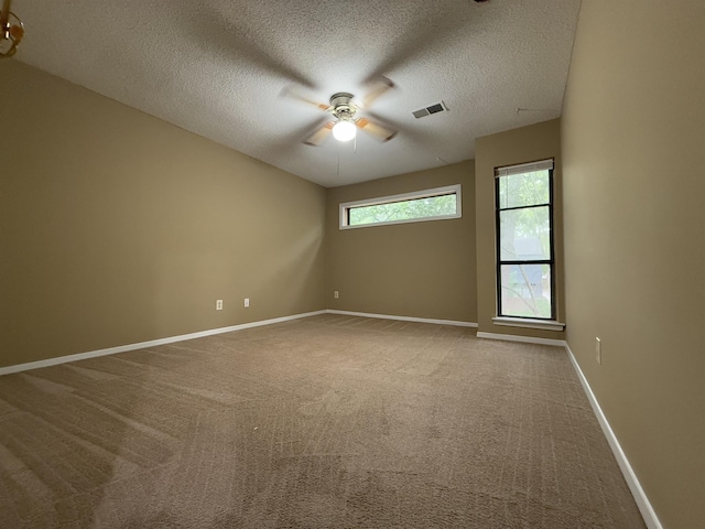empty room with carpet, a textured ceiling, baseboards, visible vents, and ceiling fan