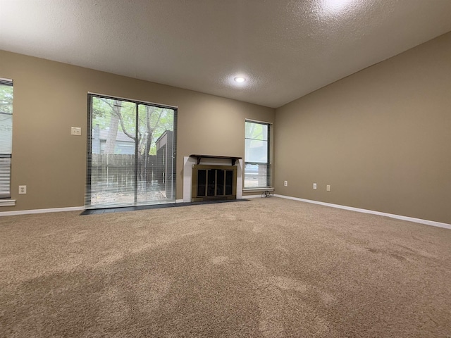 unfurnished living room featuring a textured ceiling, baseboards, a fireplace with flush hearth, and carpet floors