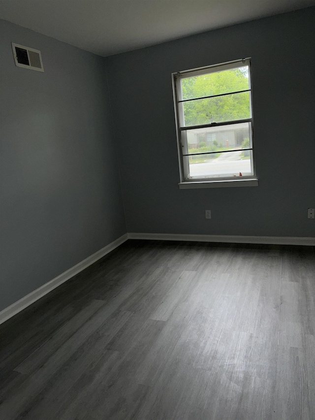 spare room with dark wood finished floors, visible vents, and baseboards