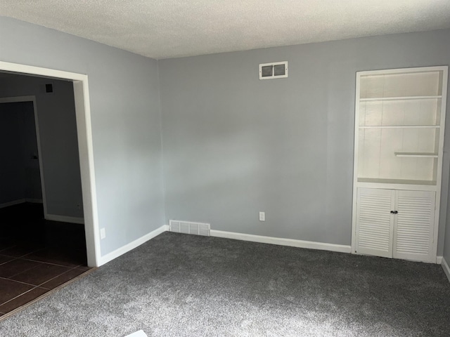 carpeted empty room with baseboards, visible vents, and a textured ceiling