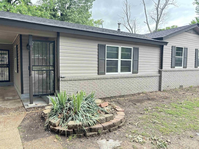 view of side of property featuring a shingled roof and brick siding