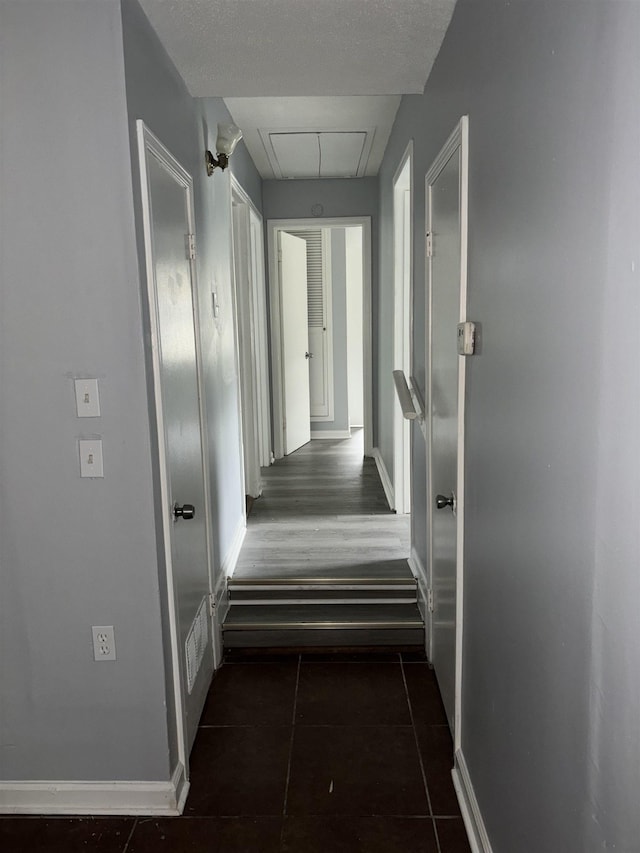 hall with attic access, baseboards, visible vents, and tile patterned floors
