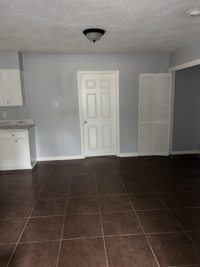 unfurnished dining area with a textured ceiling, dark tile patterned floors, and baseboards