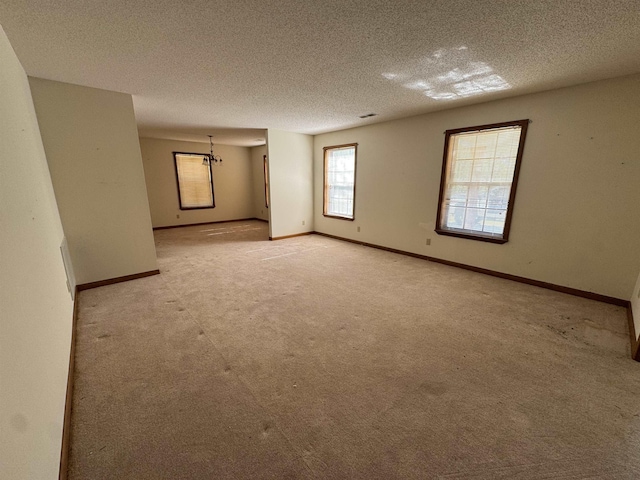 spare room with light colored carpet, a textured ceiling, and baseboards