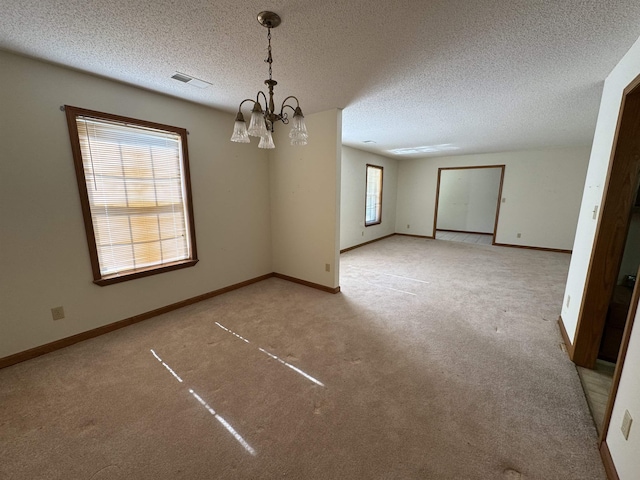 spare room featuring carpet flooring, an inviting chandelier, a textured ceiling, and visible vents