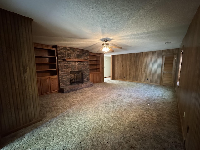 unfurnished living room with carpet flooring, a fireplace, a textured ceiling, ceiling fan, and wooden walls