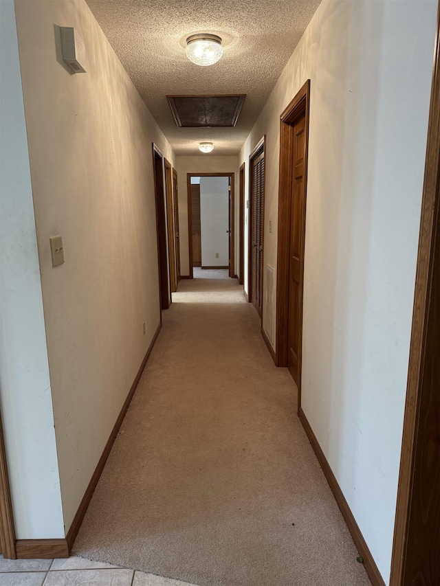 corridor featuring baseboards, light carpet, and a textured ceiling