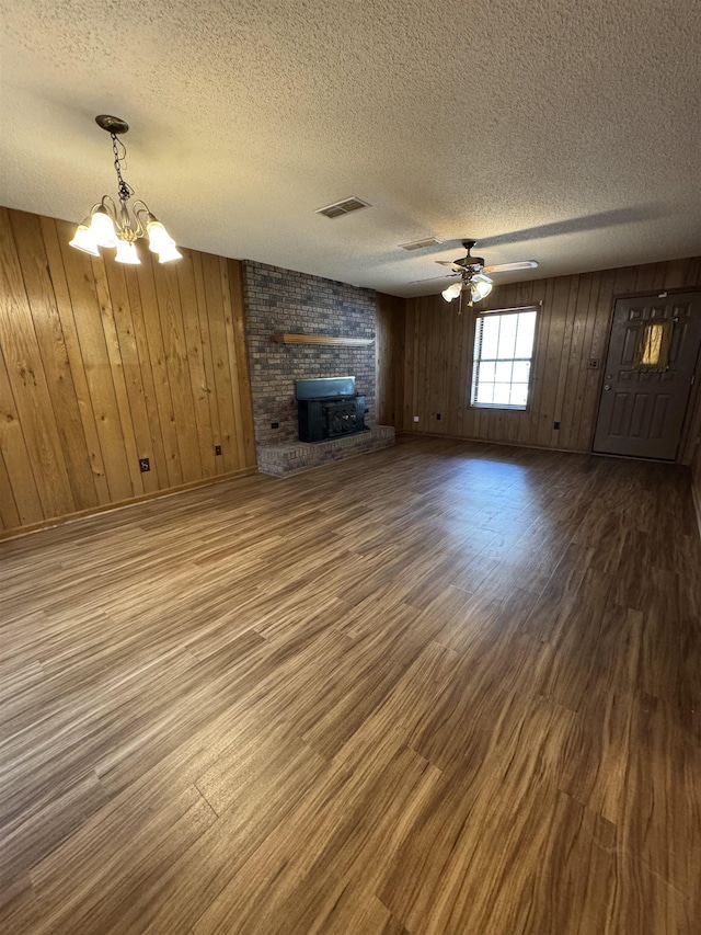unfurnished living room featuring a textured ceiling, visible vents, ceiling fan with notable chandelier, wooden walls, and wood finished floors