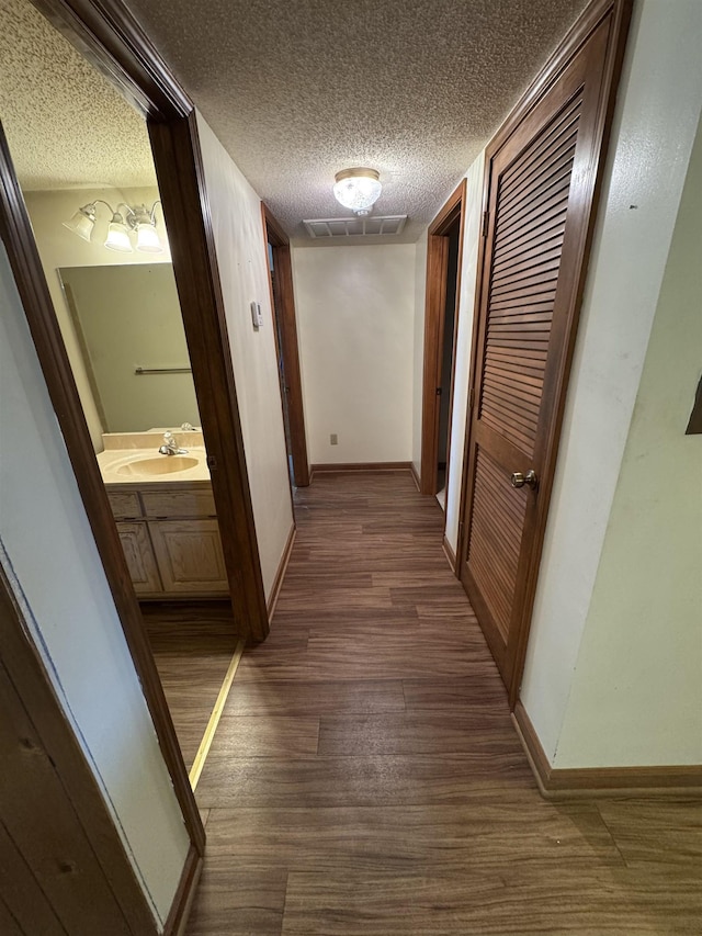 hall with a sink, dark wood-style flooring, baseboards, and visible vents