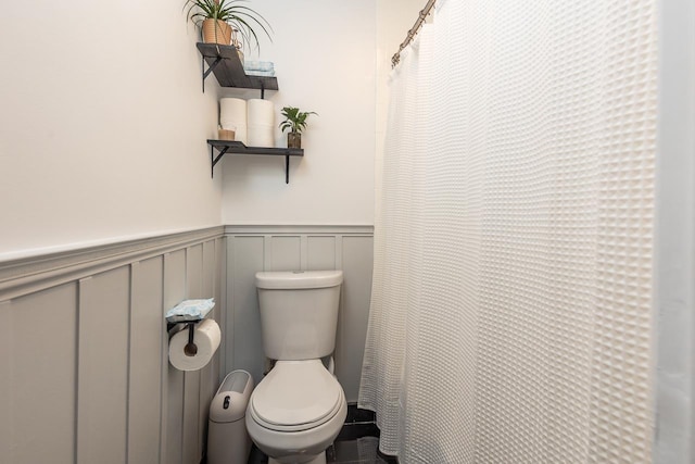 bathroom with toilet, a decorative wall, wainscoting, and a shower with curtain